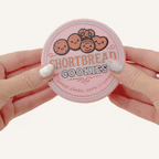 Retro tin-style clicker fidget with a working lid and textured mini sewing pieces inside for tactile play.
