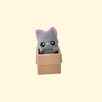 Grey kitten pop-up clicker in a faux cardboard box; tactile details, standard click with optional quiet upgrade for sensory use.
