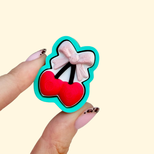 Turquoise cherry clicker with heart cherries and shiny bow detail, a satisfying press fidget for focus and stress relief.

