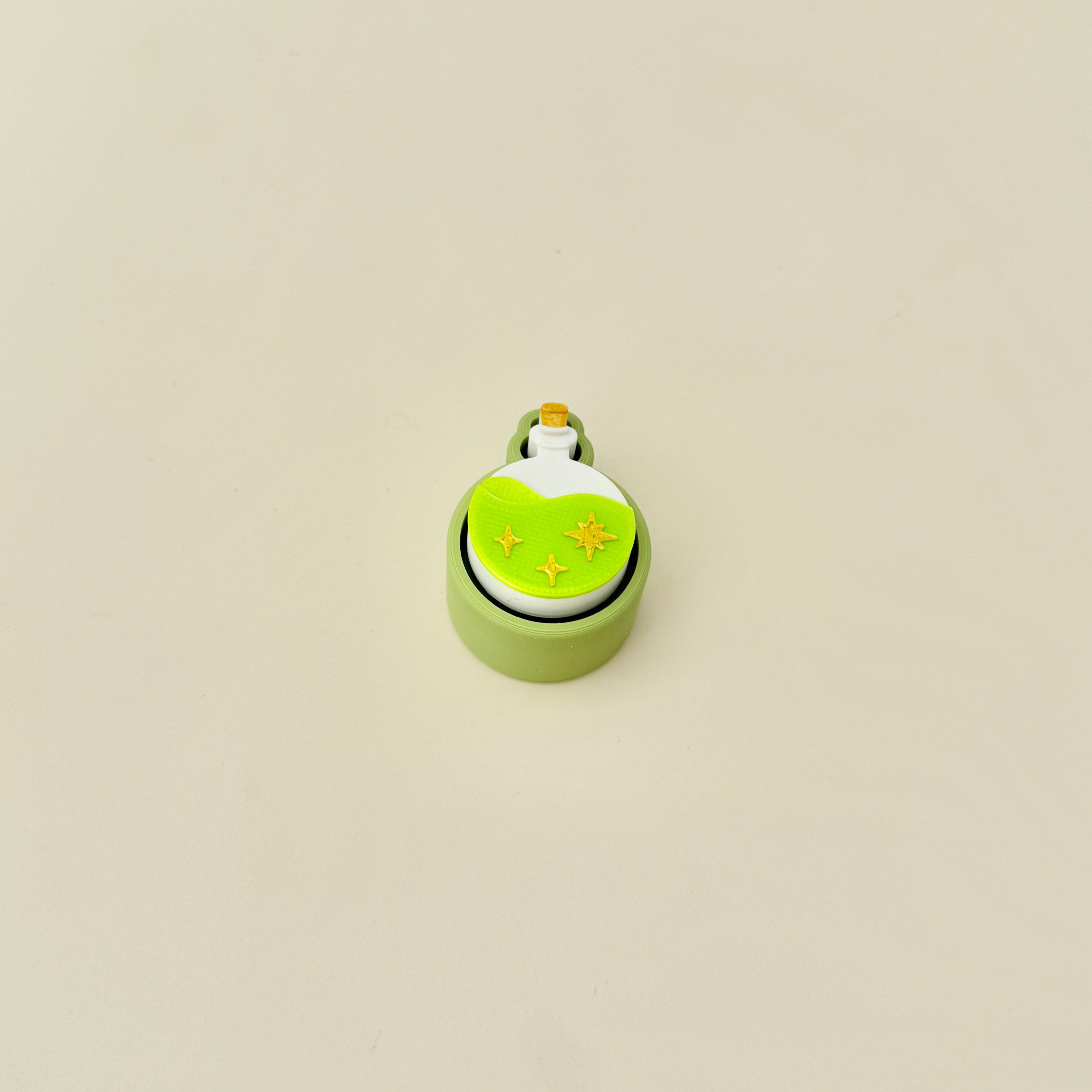 Sensory tool with a textured top and central click feature in a magical potion theme