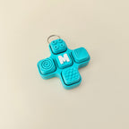 Blue fidget spinner keychain with textured surface and letter 'M' on a beige background