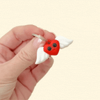 A vibrant red heart keyring with black eyes, a smile, and white moving wings.