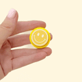 round fidget clicker with raised face icon and textured rim
