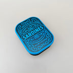 Handheld tin fidget featuring three press-to-click sardines and varied textures for sensory input and grounding.
