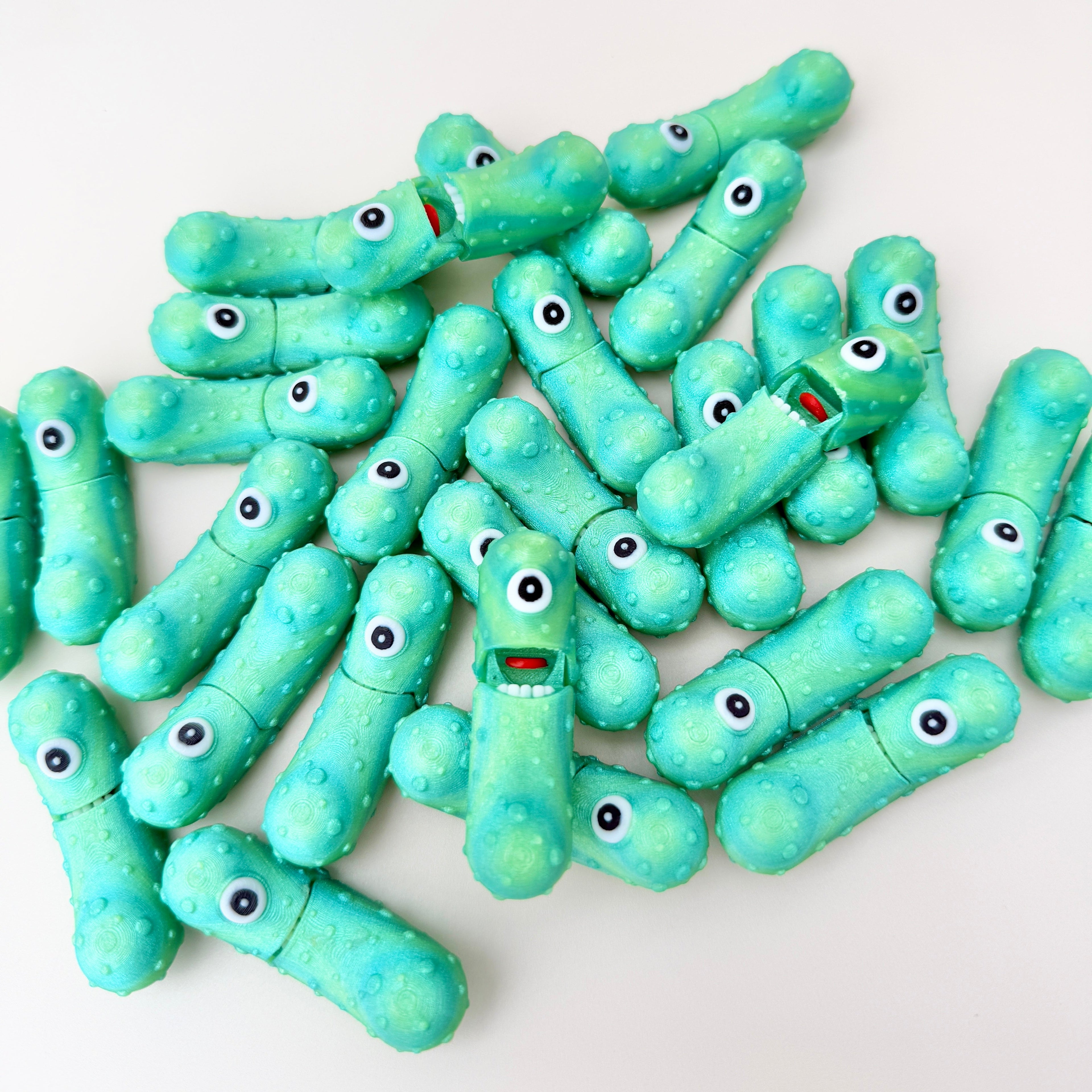 A shimmering green pickle-shaped toy with a single eye and an opening mouth for sensory play.