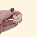 mini bow-shaped clicker with smooth top and metal loop for attaching to keys or bags
