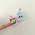 A miniature shelf-style clicker fidget with a keyring loop and one chosen icon inside.

