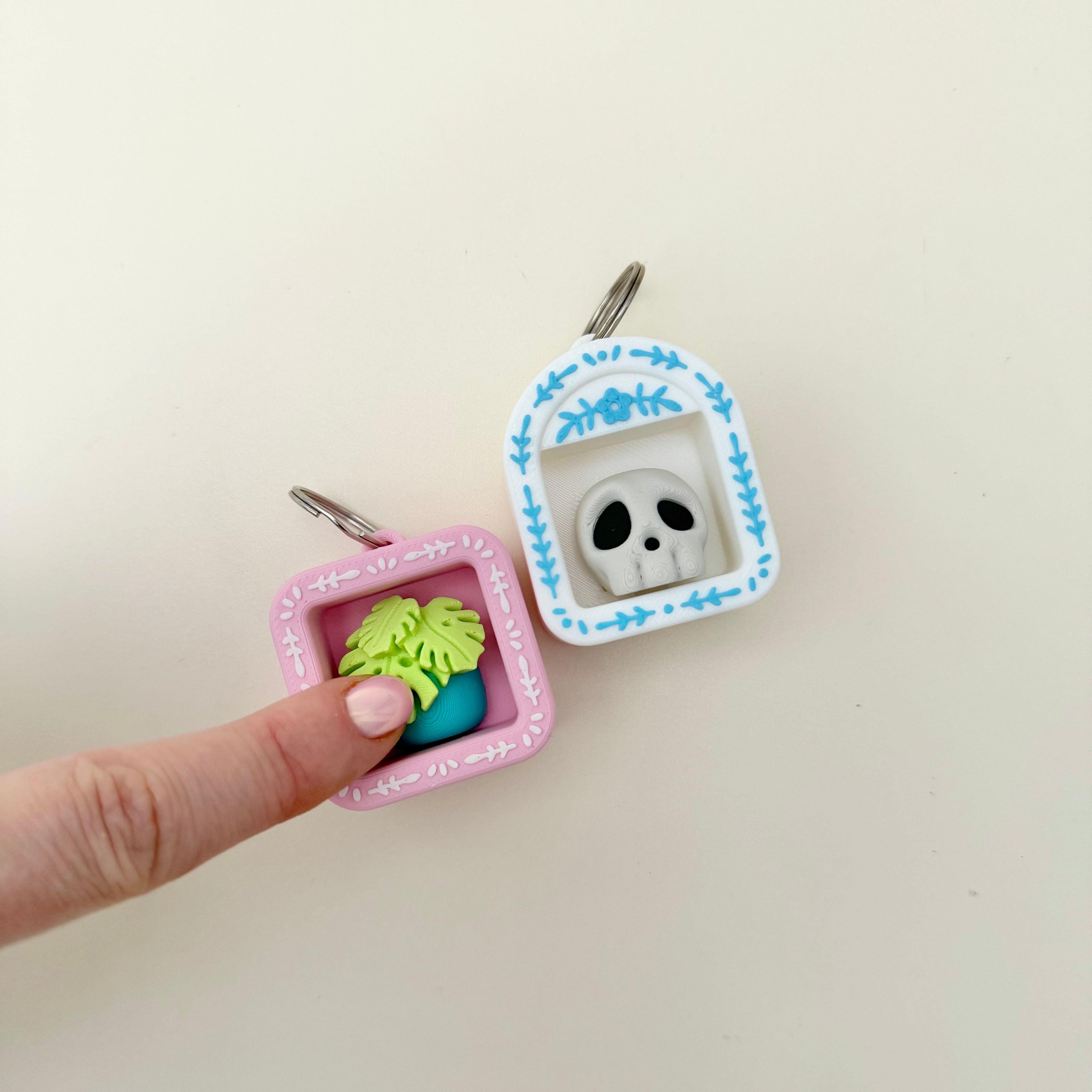 A miniature shelf-style clicker fidget with a keyring loop and one chosen icon inside.
