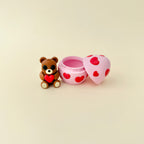 A pink and red heart-patterned egg that doubles as a carry case for a teddy bear fidget toy.