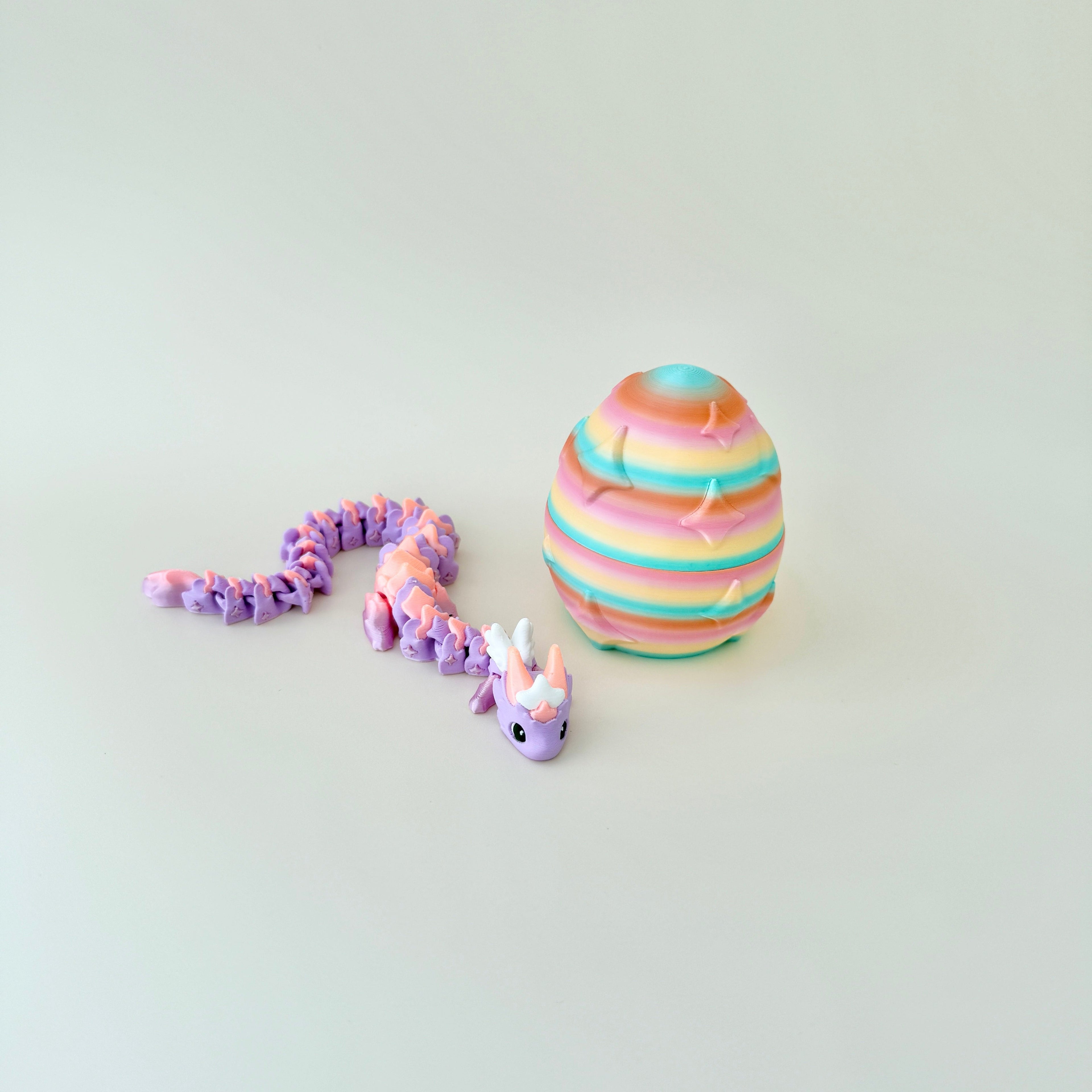 Gradient lilac and peach dragon resting beside a rainbow egg embossed with twinkling stars.