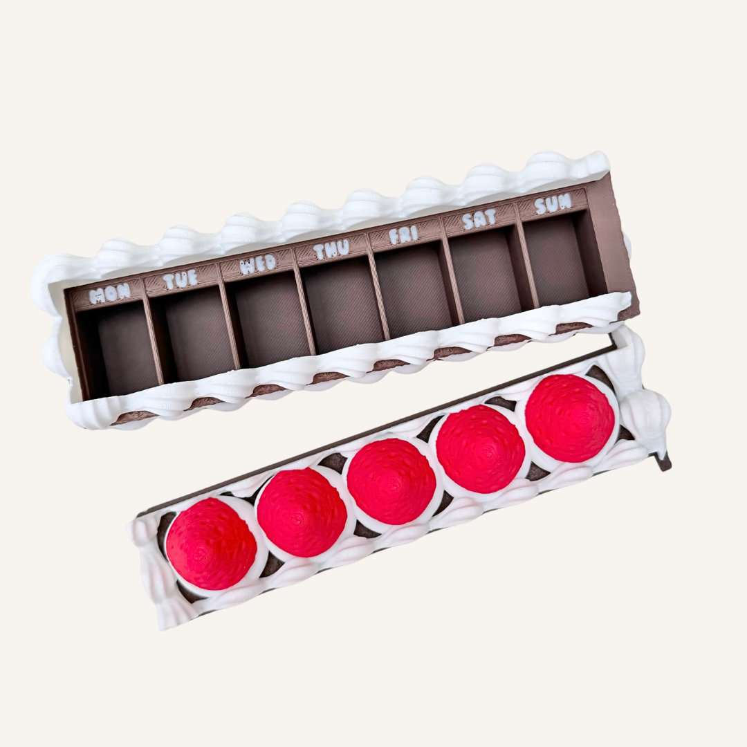 Weekly pill box with sliding lid and daily compartments for medication or vitamins in a cute cake design.
