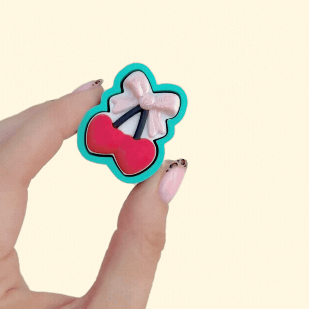 Handheld clicker fidget with bold casing and cute heart-cherry design, made for calming repetitive clicking.
