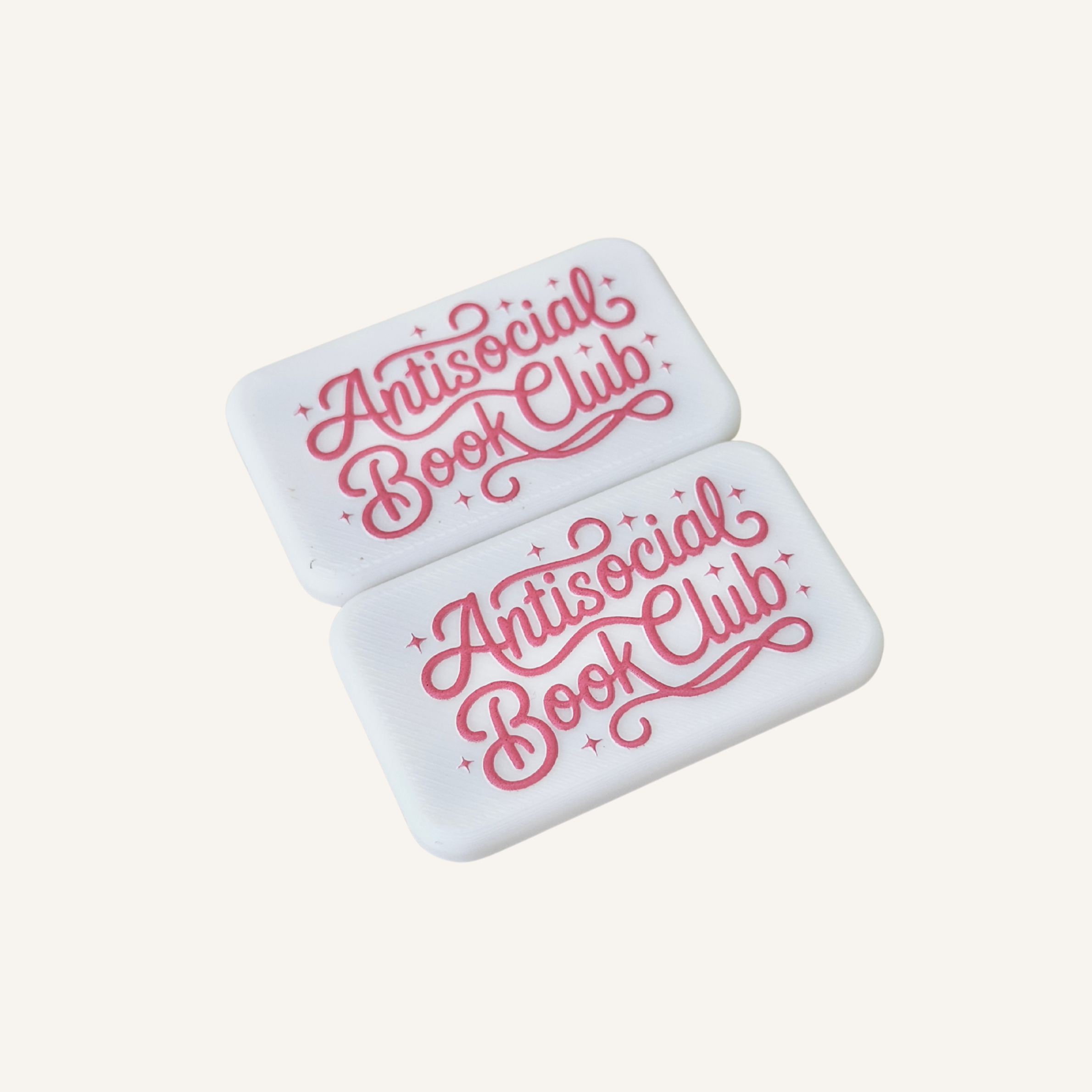 Pair of white magnetic sensory fidgets with raised pink Antisocial Book Club artwork.