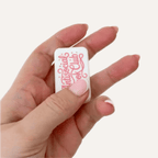 White Antisocial Book Club magnetic sensory fidgets held in hand with raised pink lettering on the front.