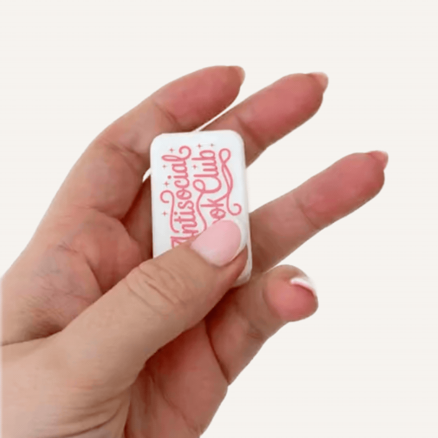 White Antisocial Book Club magnetic sensory fidgets held in hand with raised pink lettering on the front.