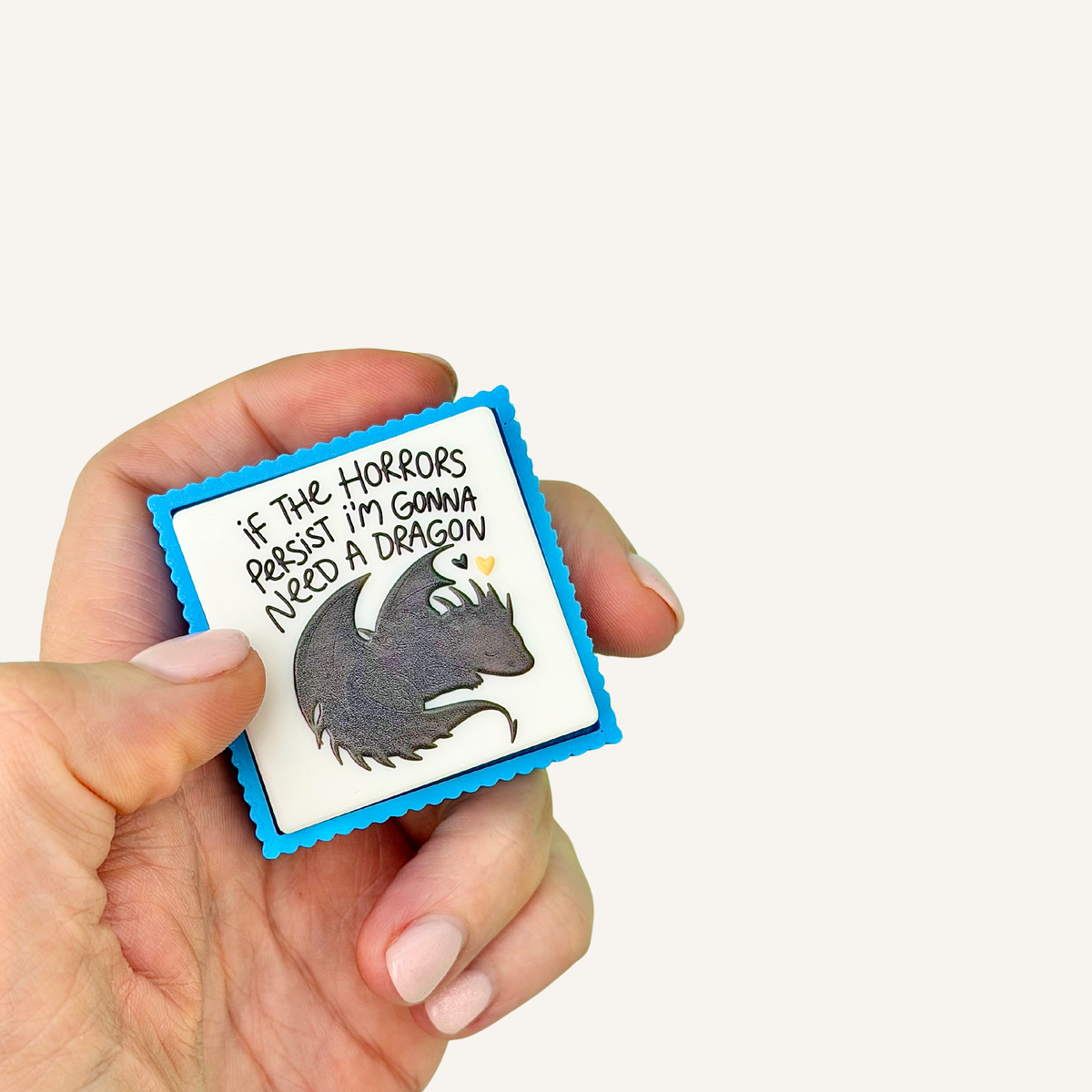 Chunky blue and white Need a Dragon sensory clicker with raised dragon artwork and tactile ridged edges.