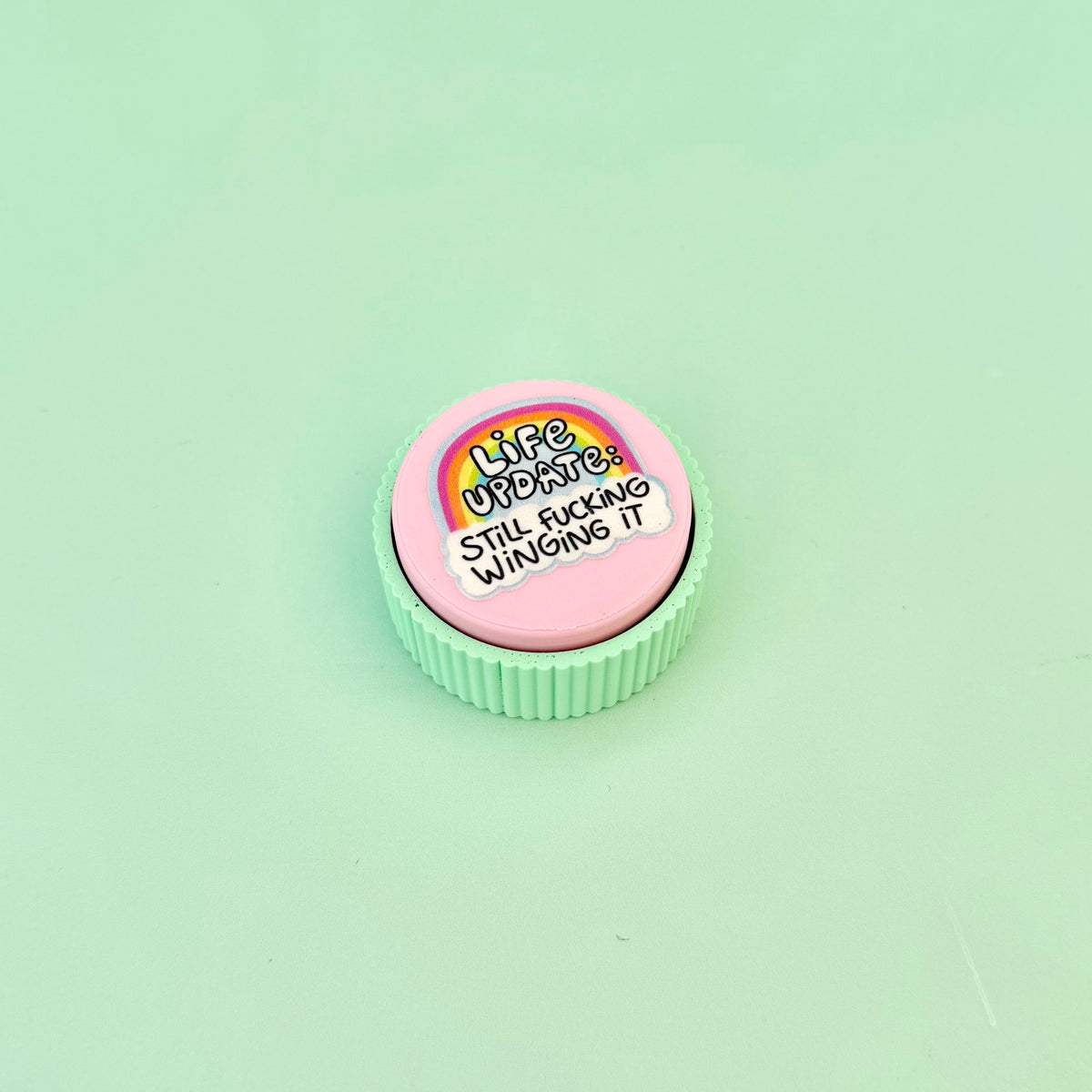 Pink and mint handheld sensory clicker with tactile outer ridges and raised colourful artwork.